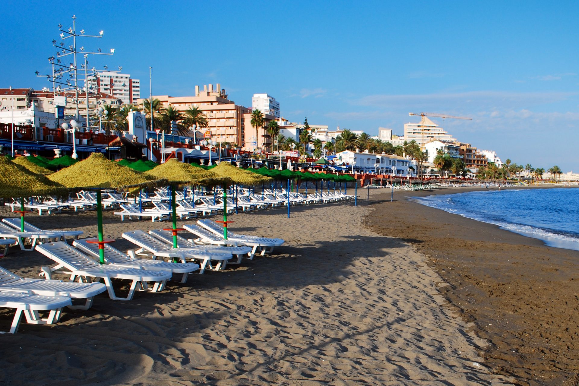 Het strand en de boulevard van Benalmádena Costa, met ligbedden, palmen en appartementengebouwen op de achtergrond