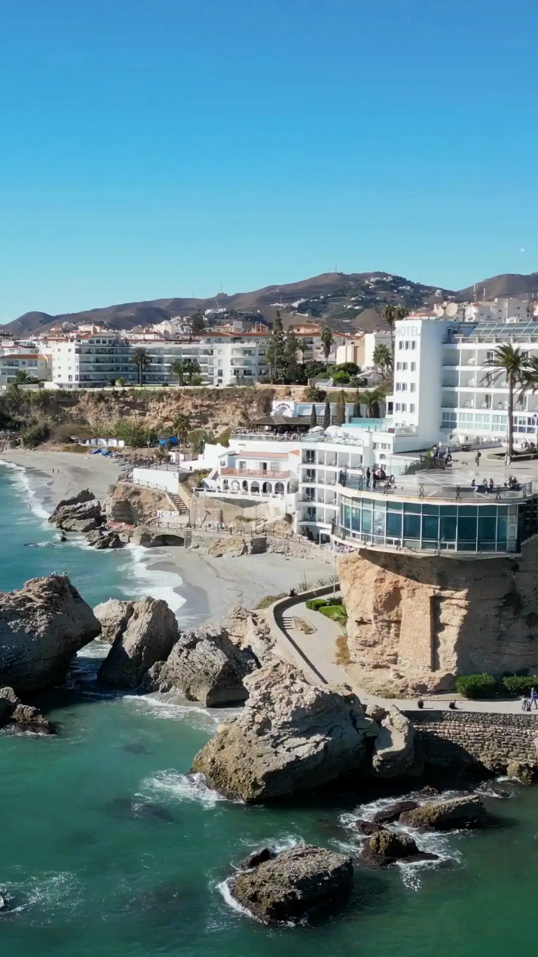 Aerial view of a beach lined with palms, with apartment buildings behind